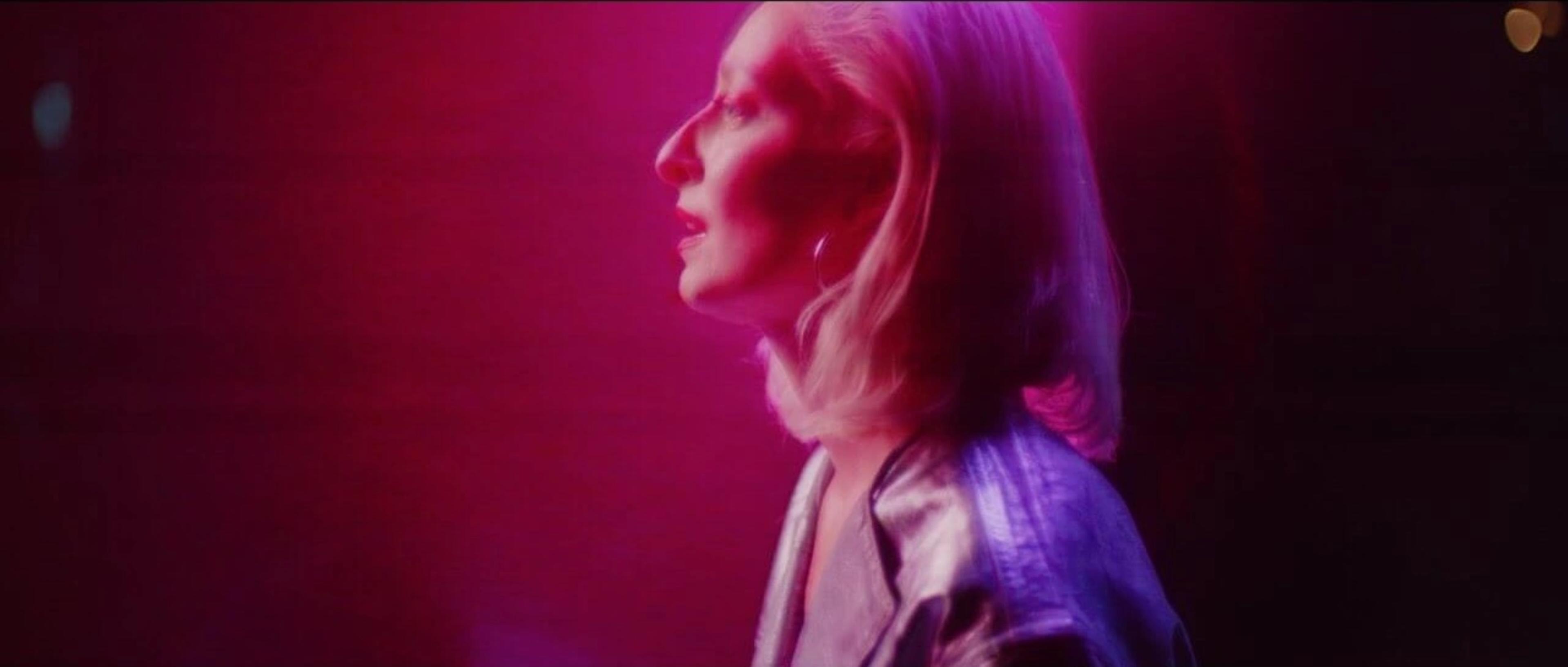 A neon-soaked, pinkish-purple-toned scene from the music video 'UNSUNG', directed by Martyn Thomas, featuring a singer in profile under strobe lighting.